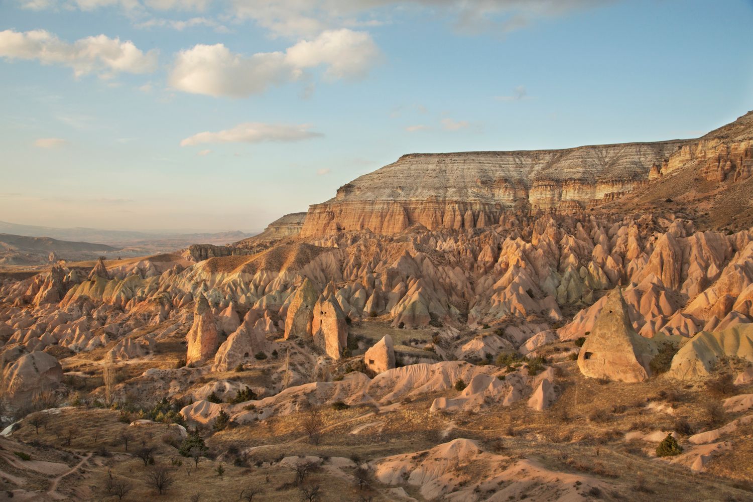 Golden sunlight illuminates layered rock formations in desert valley under blue skies.
