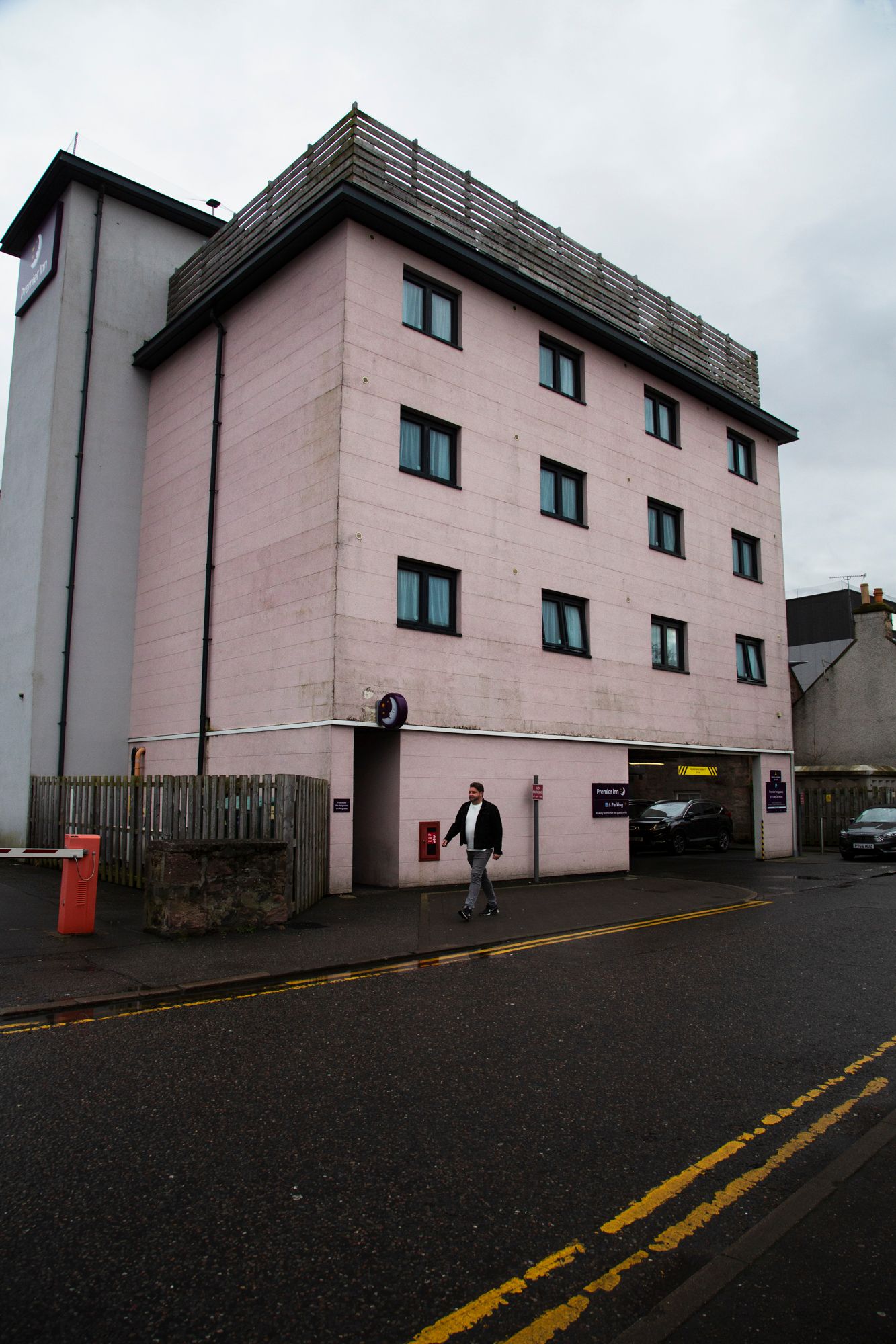 Pink apartment building exterior with dark asphalt parking lot and yellow road markings on an overcast day.