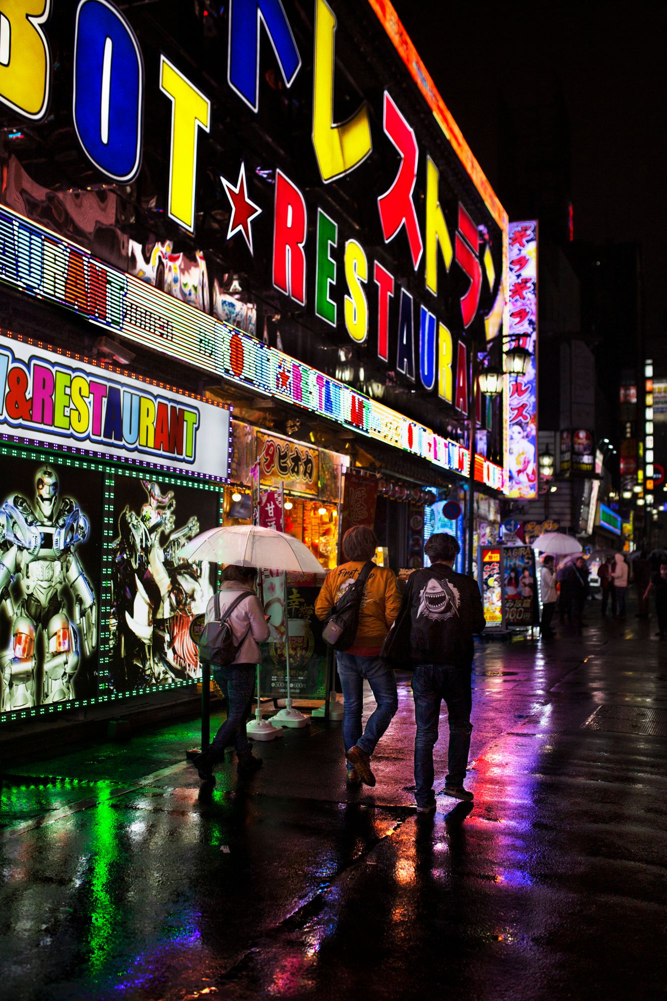 Vibrant neon signs reflect on wet pavement in a Japanese entertainment district at night.
