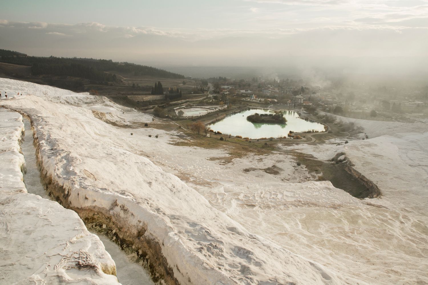 Aerial view of white calcium terraces and thermal pools in mountainous landscape.