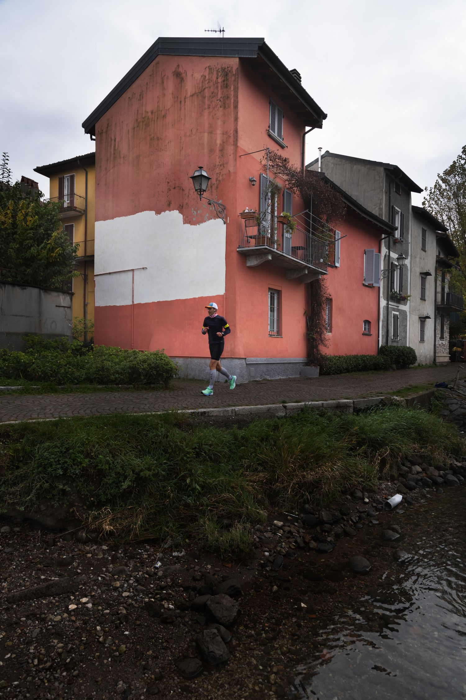 A jogger runs along a riverside path beside a pink building in a European town.