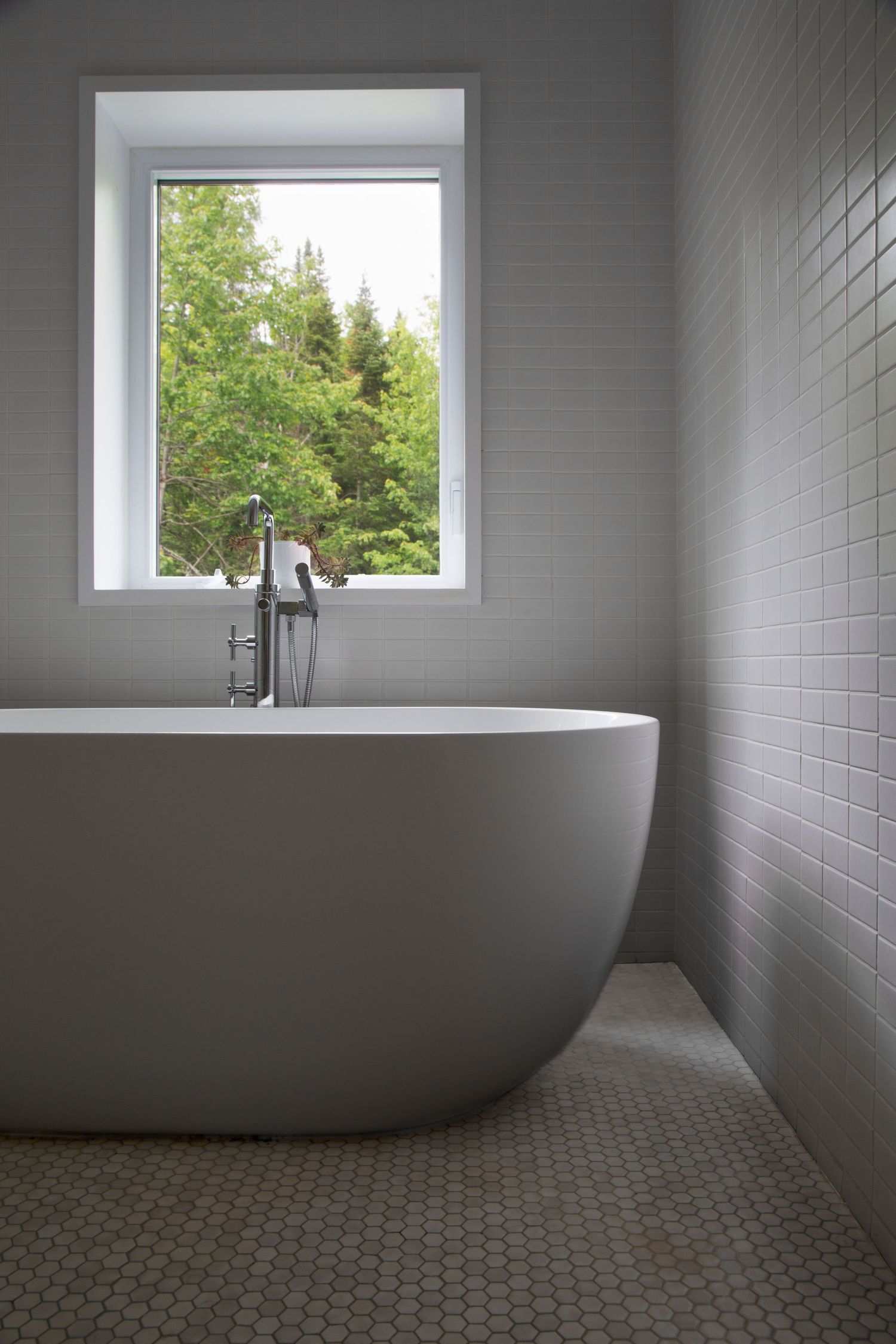 Minimalist bathroom featuring a freestanding tub, white tile walls and natural light from window.