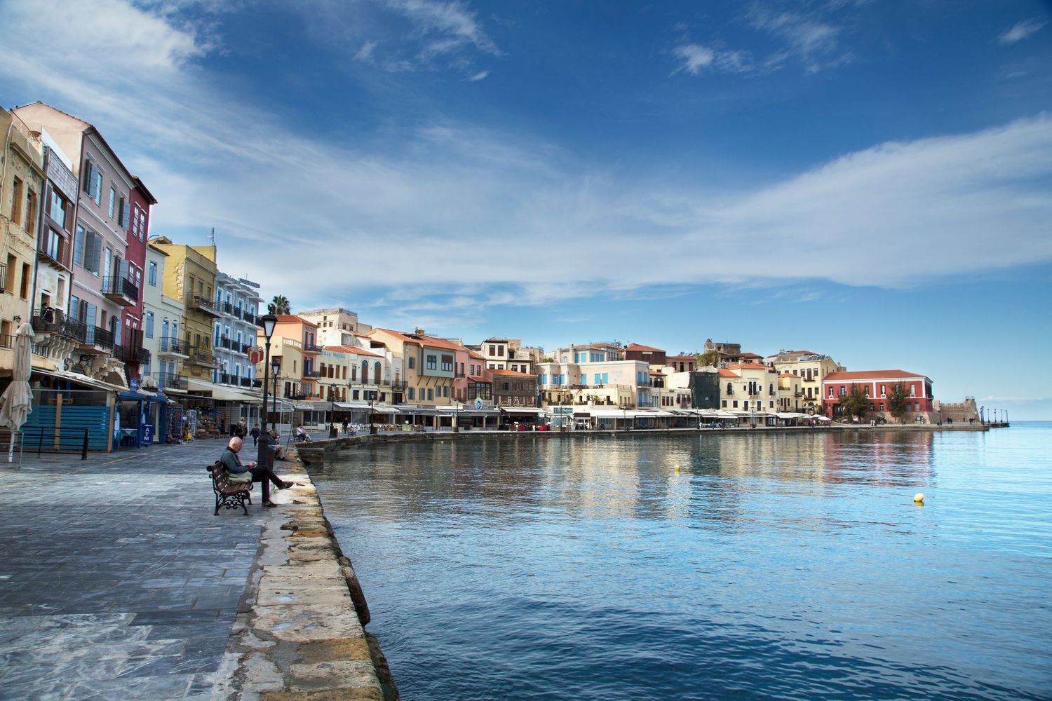 Panoramic view of colorful buildings along a Mediterranean waterfront with blue sky and calm waters.