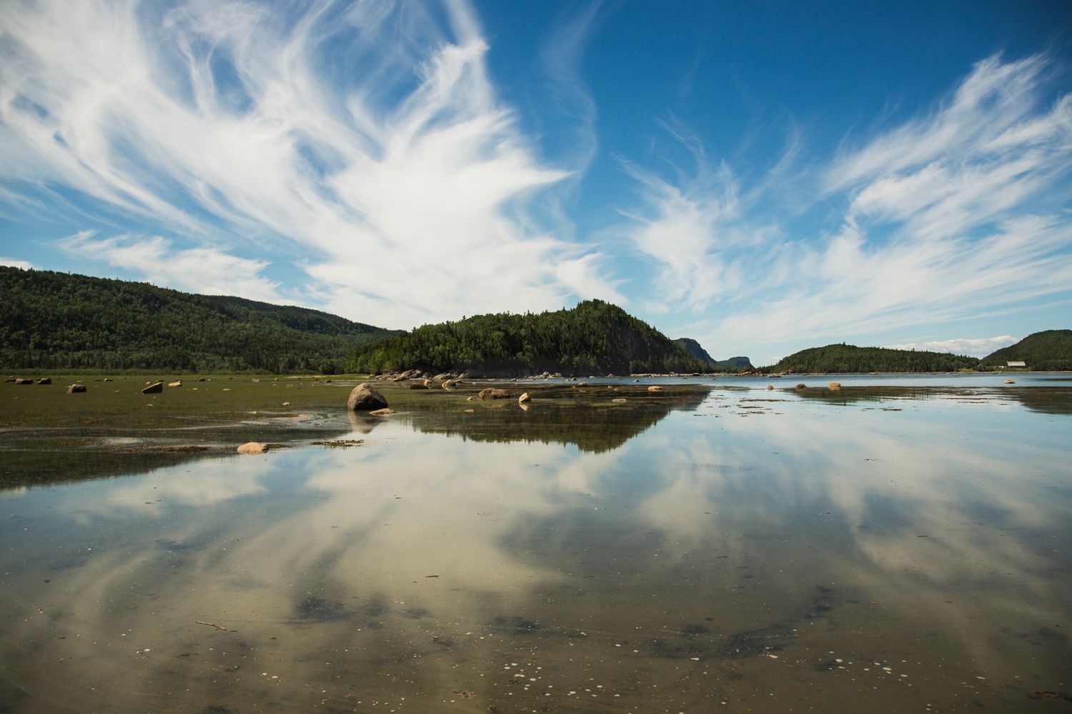 Reflective lake surface mirrors dramatic cloud formations under blue summer sky.