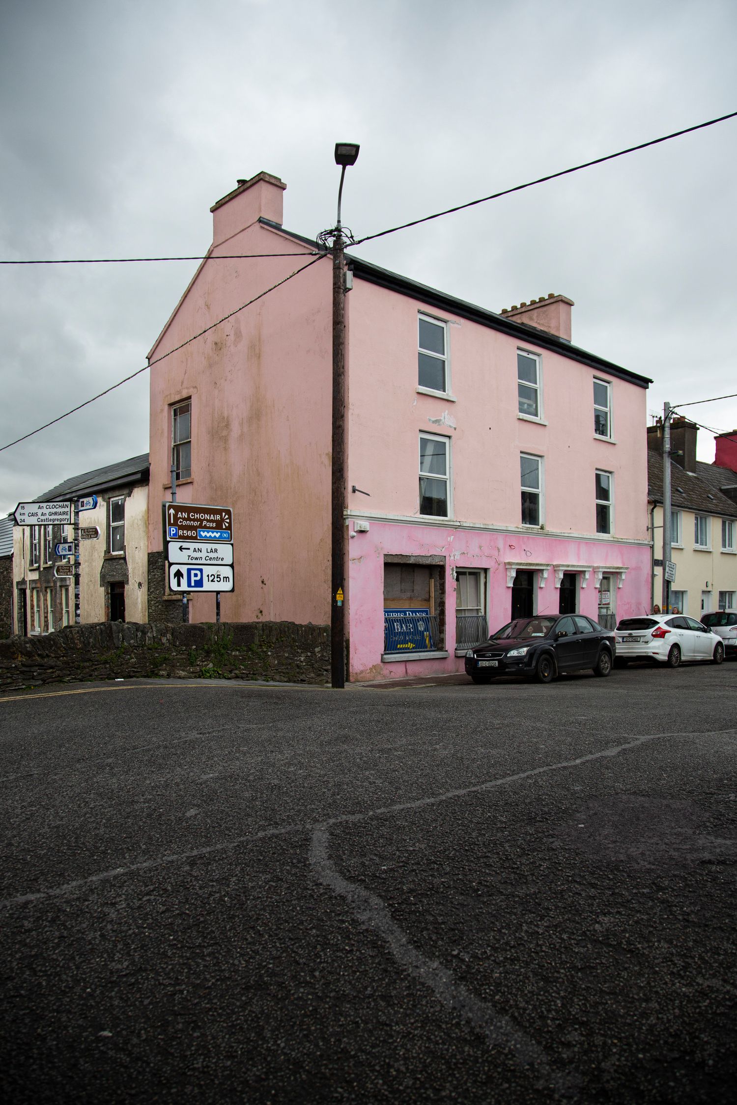Pink-colored buildings line a quiet street corner in an Irish coastal town.