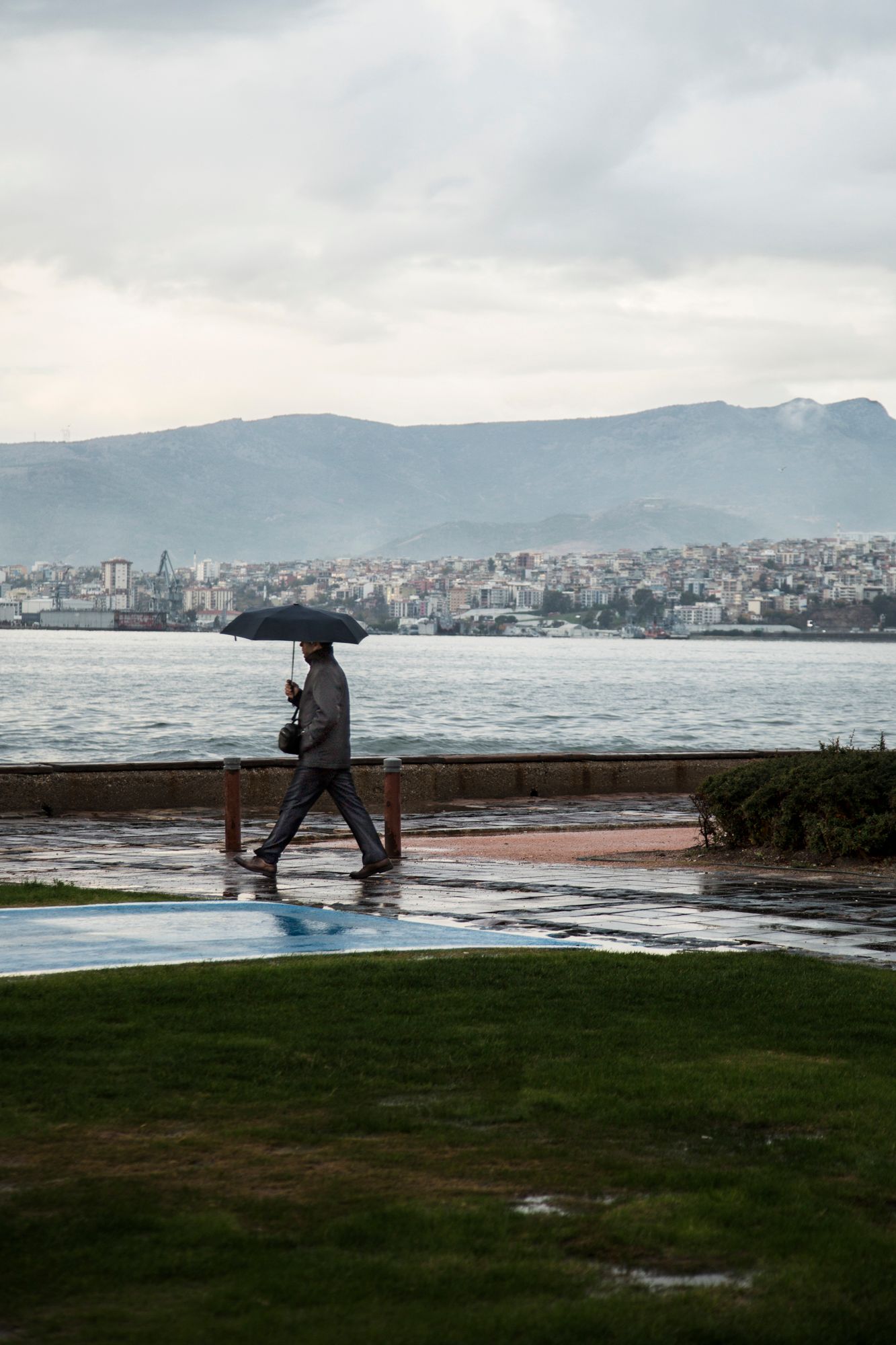 Storm waves crash against a seawall with dramatic cloudy skies and city skyline in the background.