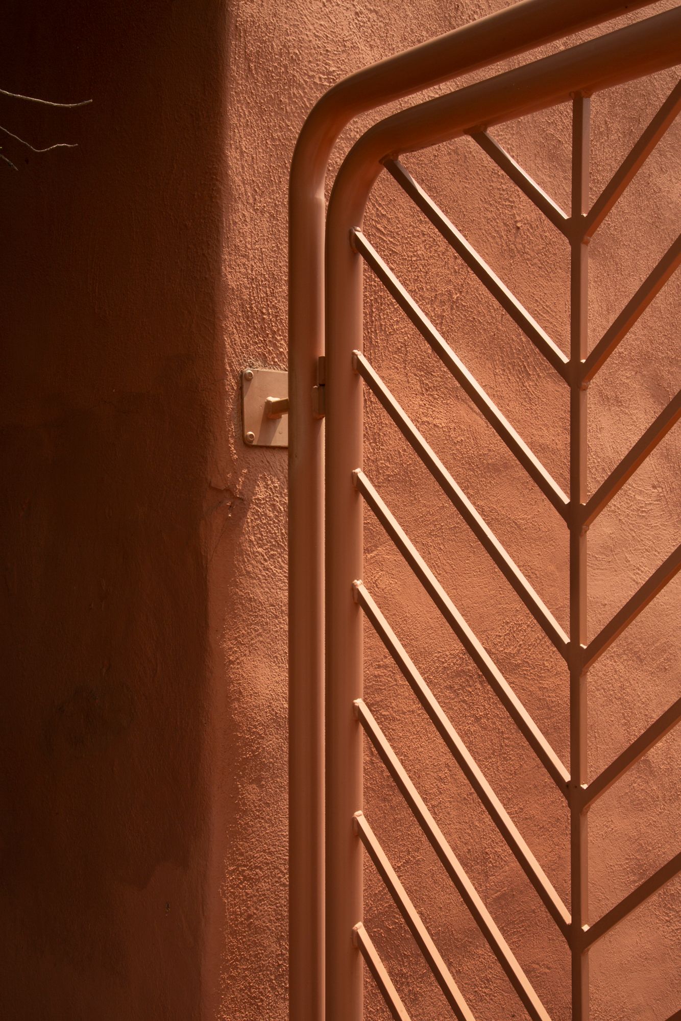 Geometric pattern of light and shadow created by sunlight through chevron-shaped window frames on a textured wall.