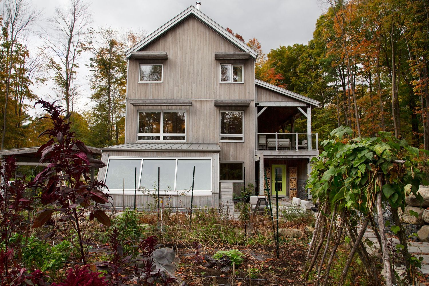 Modern wooden house with minimalist design sits among autumn trees on a sloping landscape.