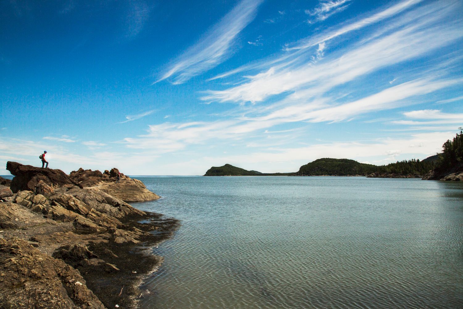 Rocky coastline panorama with calm blue waters and dramatic cloud formations stretching across the horizon.