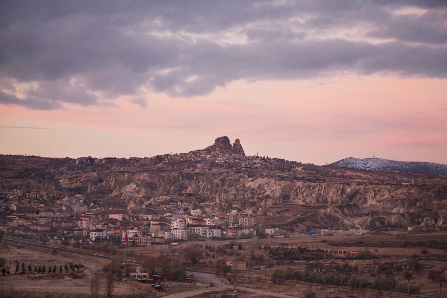Pink sunset illuminates a hillside town built among rocky terrain in Cappadocia.