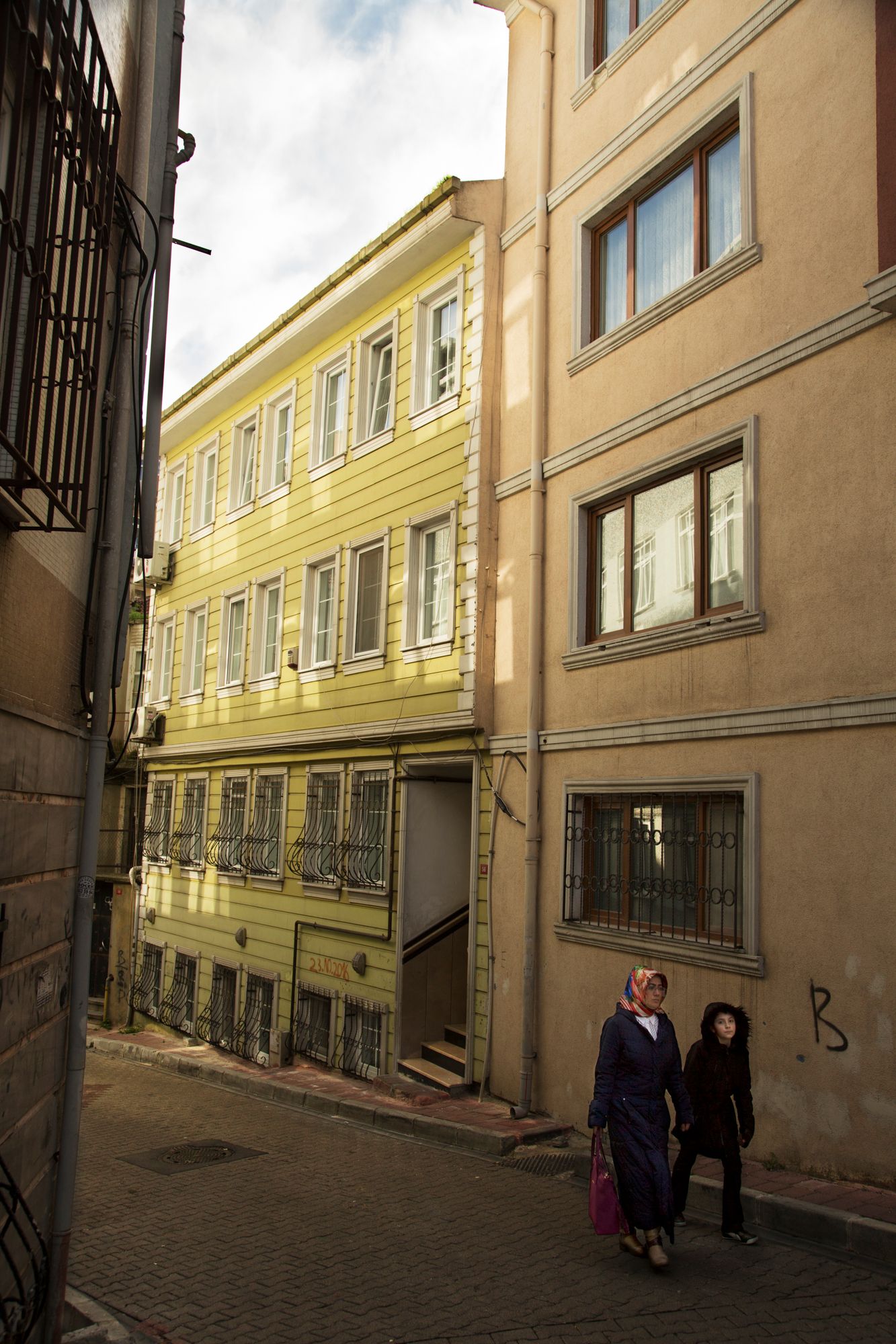 Narrow alley between yellow and beige buildings with traditional architecture in old city neighborhood.
