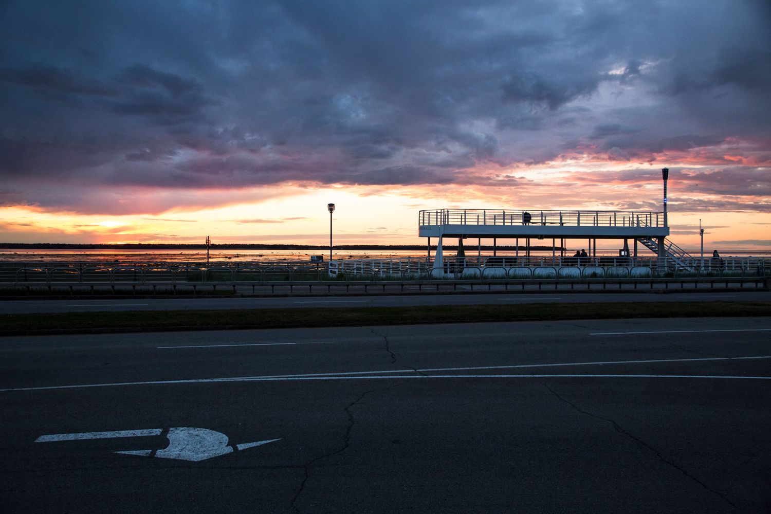 Dramatic sunset panorama over waterfront with silhouetted structures against colorful sky.