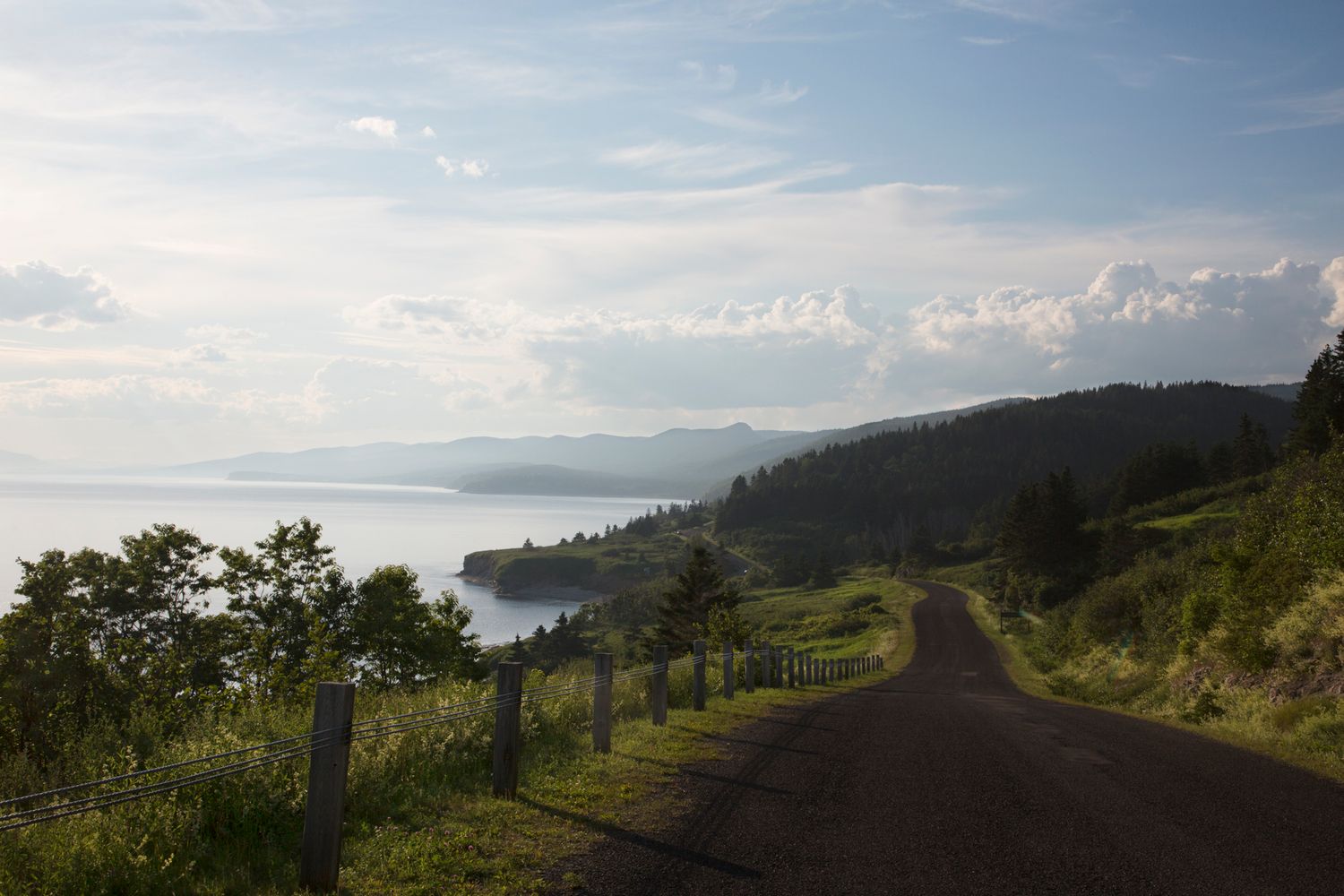 Winding dirt road along a coastal hillside with scenic ocean views and distant mountains.