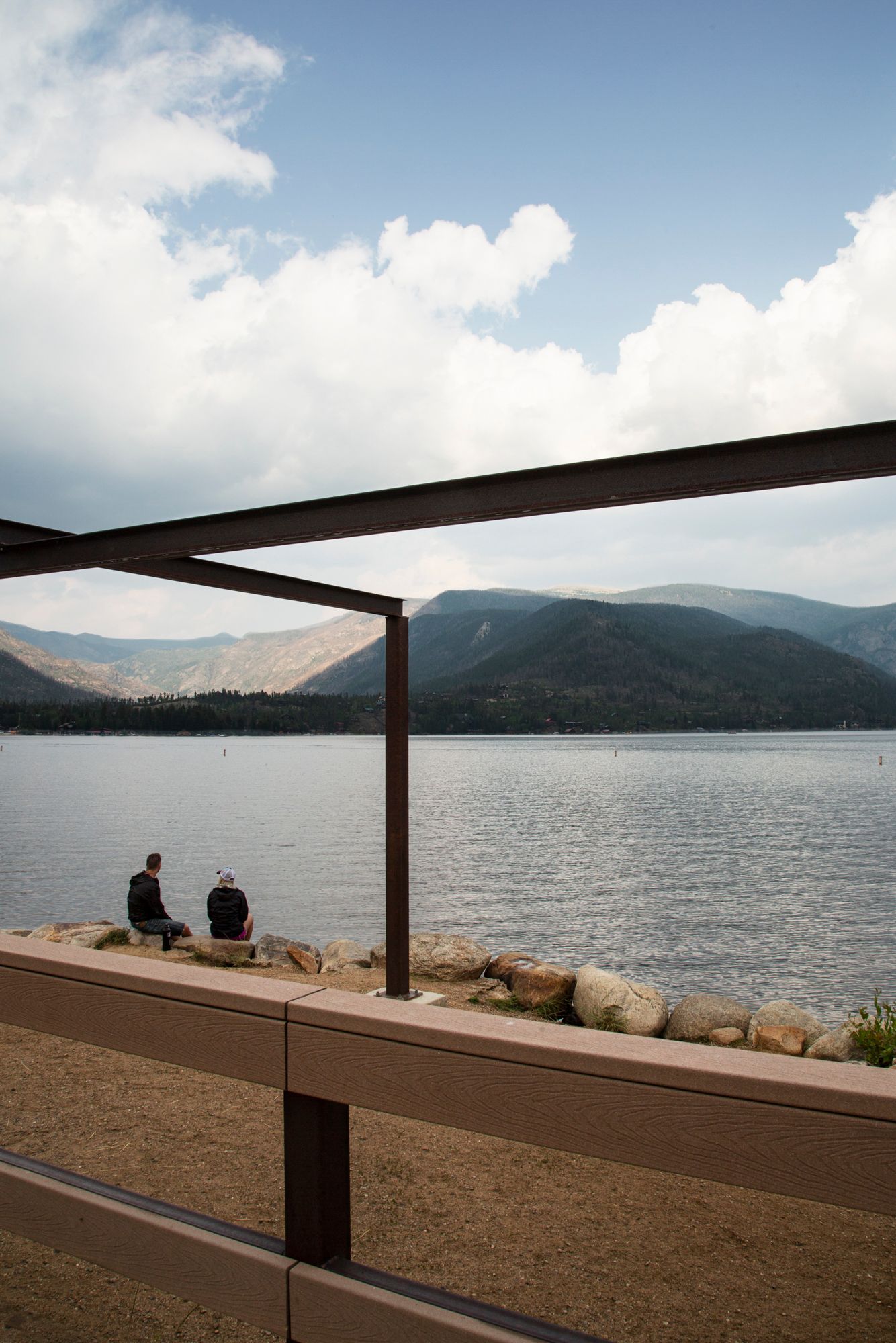 A panoramic view of a lakeside deck with geometric pergola framing the mountain landscape and water views.