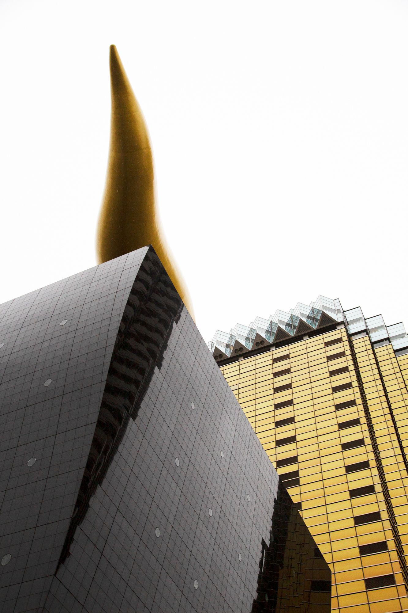 Modern architectural detail of black and gold skyscraper facade against white sky.