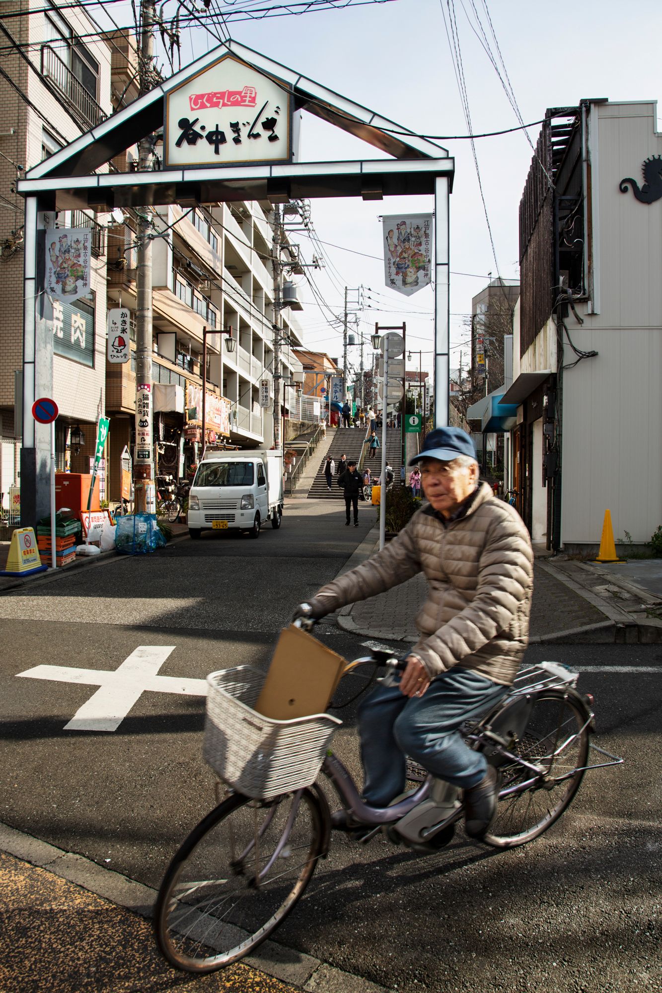 A cyclist navigates through a residential street with power lines overhead in Japan.