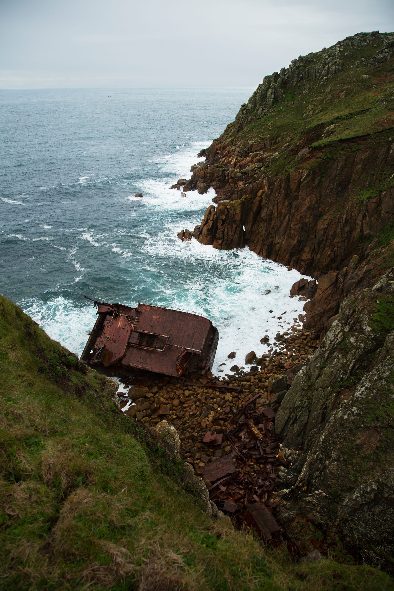 Dramatic cliffside view of a shipwreck rusting against rocky coastal outcrops.