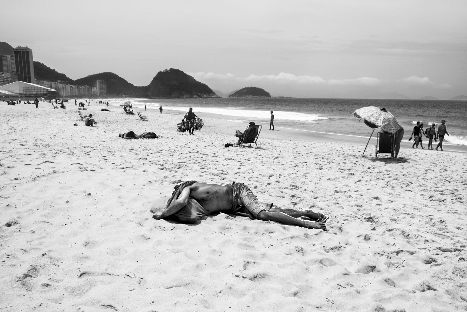 Black and white photograph of a scenic beach with mountains visible in the distance.