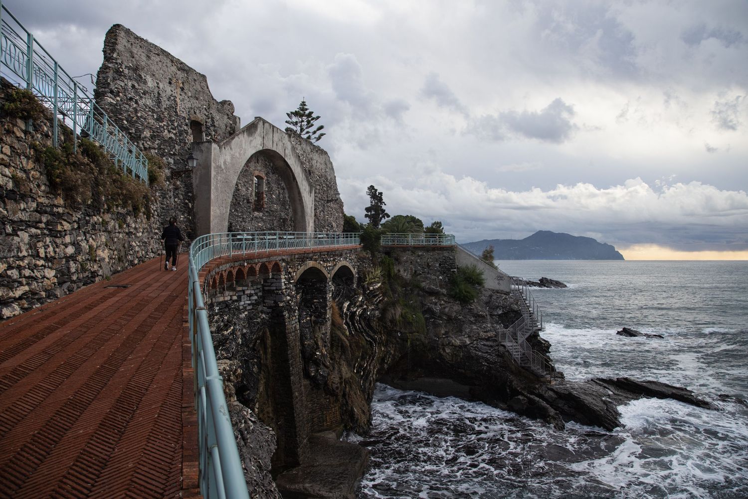 Coastal walkway with stone arch bridge over rocky cliffs and stormy sea, Cinque Terre, Italy.