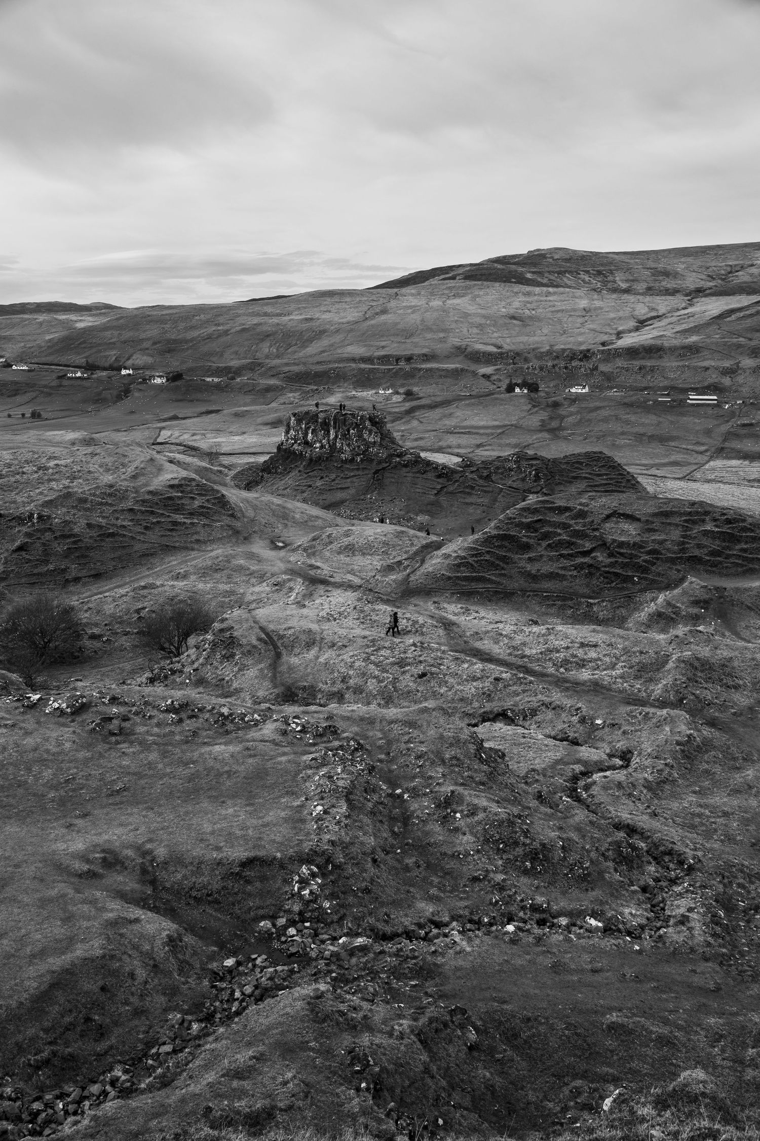 Aerial black and white photograph of a rocky hillside terrain with scattered buildings in the distance.