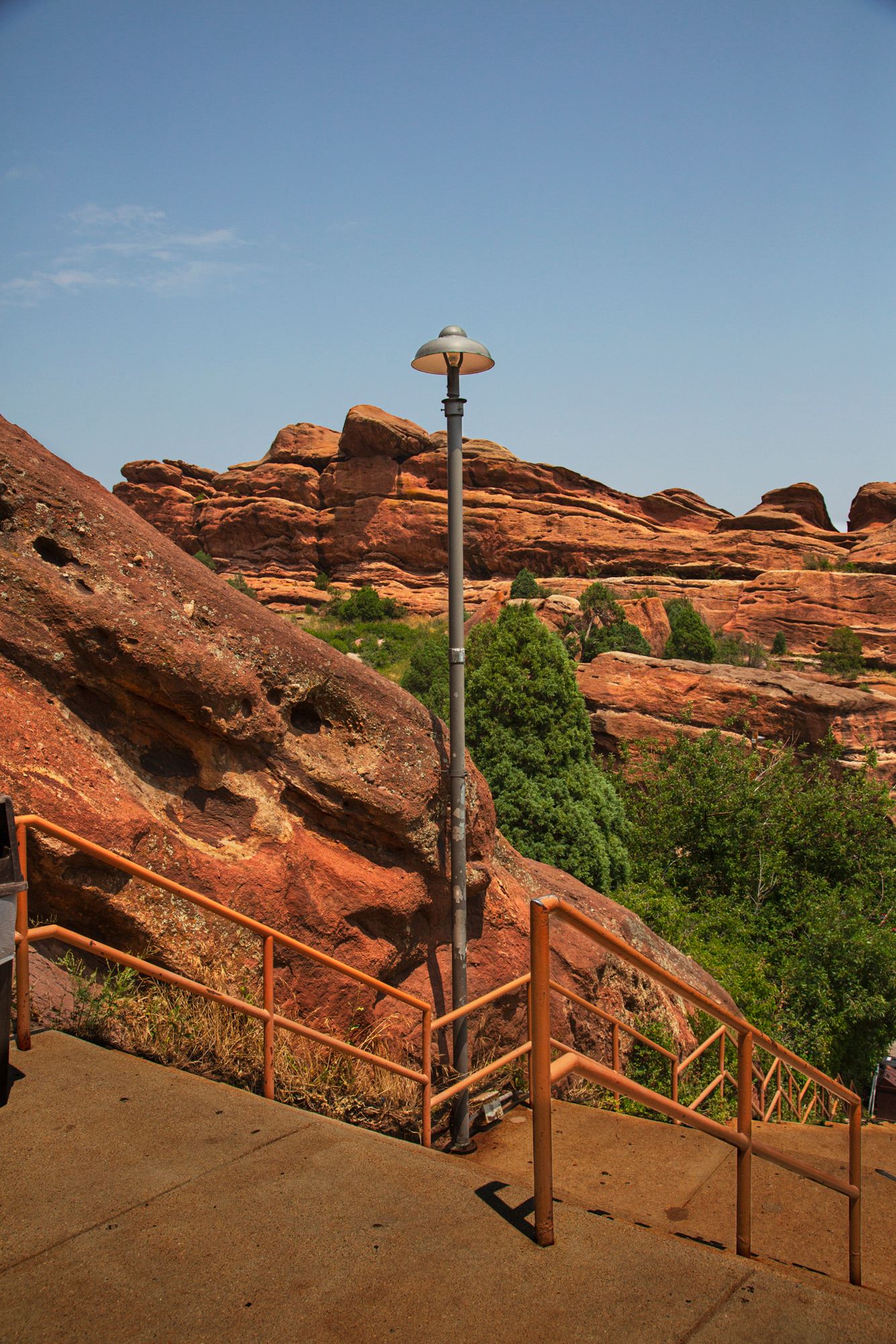 Wooden stairway and handrails lead up steep red rock formations at Red Rocks Park in Colorado against a blue sky.