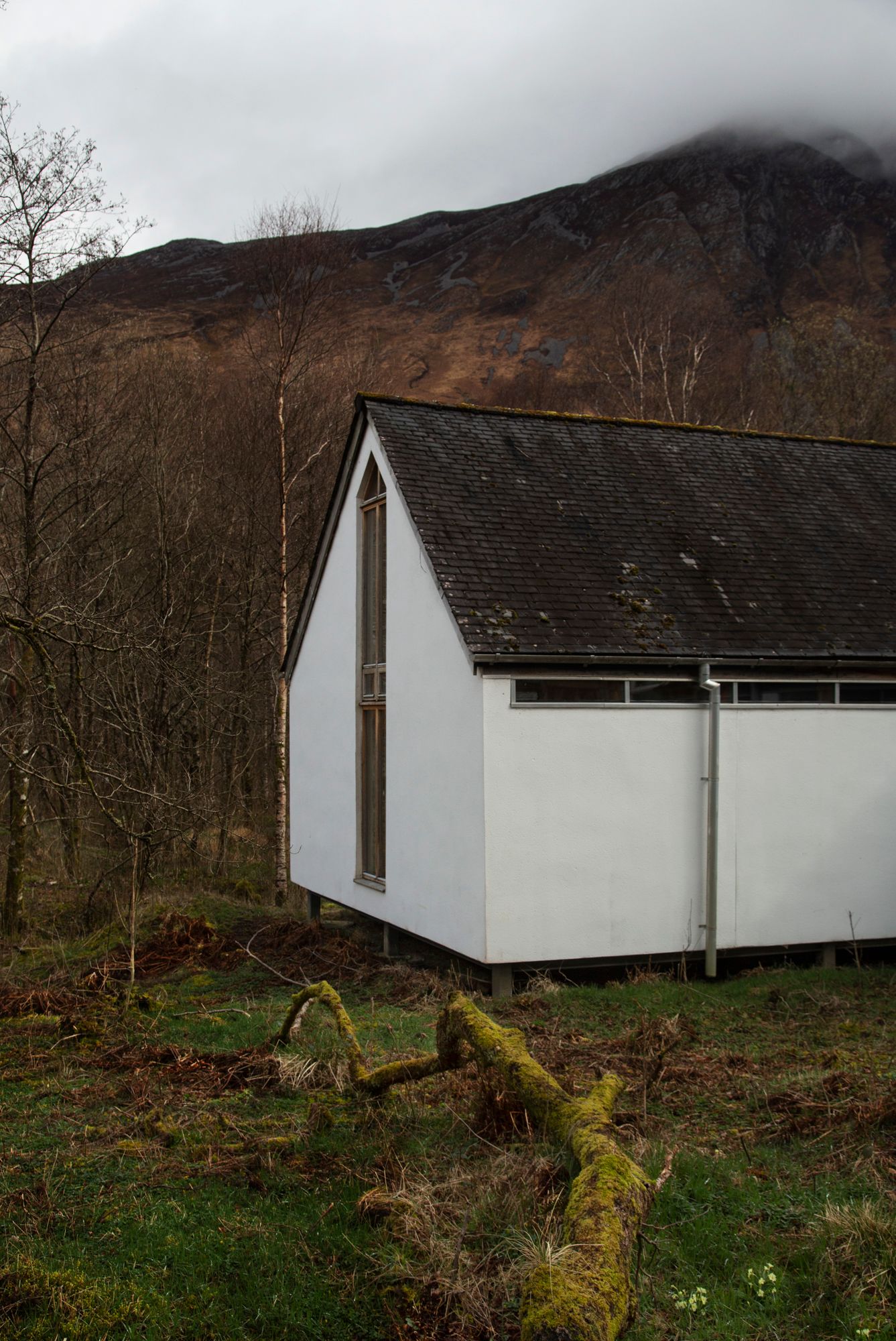 A white modular building with windows sits against a backdrop of rugged Scottish mountains and bare winter trees.