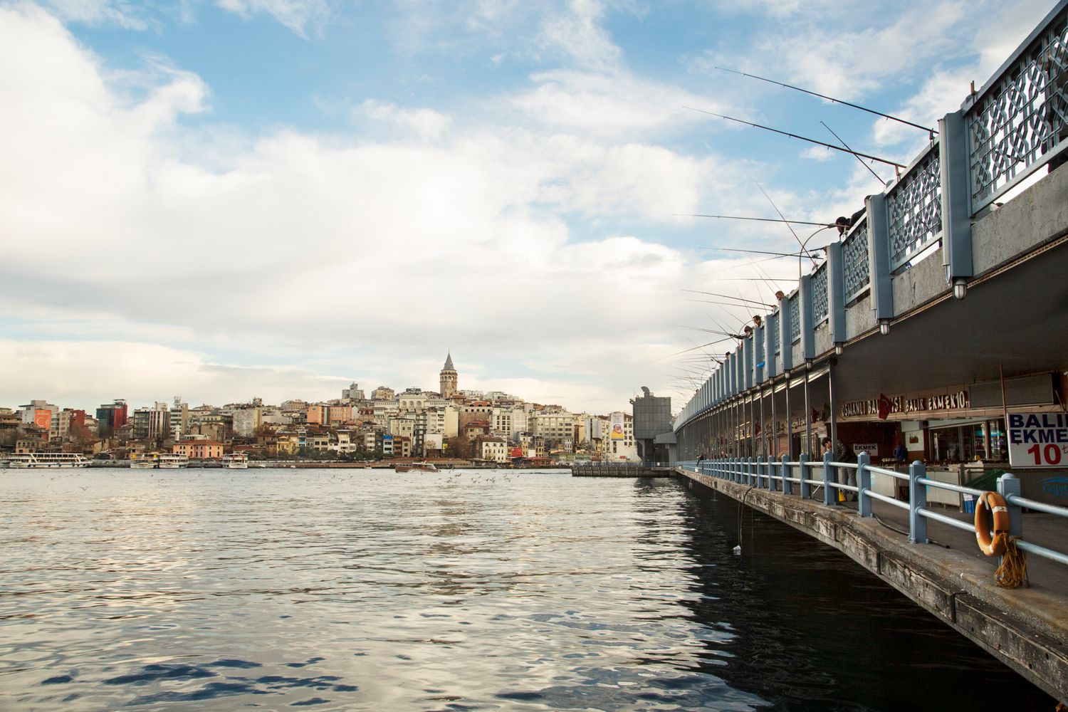 Waterfront promenade with modern pier extending into the sea under blue skies.