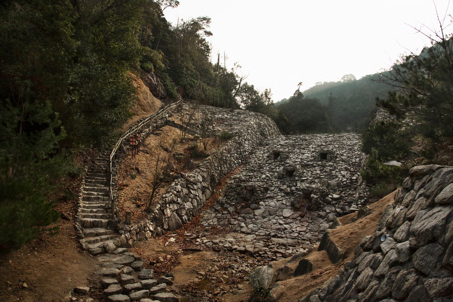 Stone steps lead up a rocky mountain path with rustic handrails.