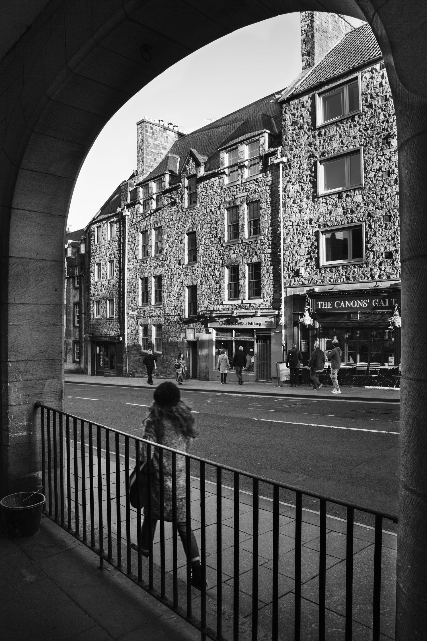 Stone buildings with archways along a quiet street viewed through a dark corridor.