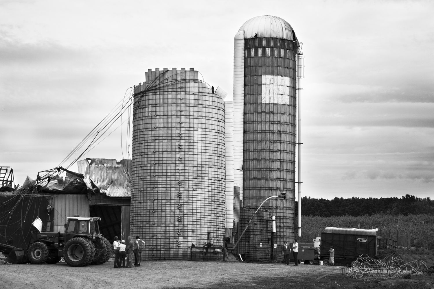 A black and white panoramic collage showing various farm silos and agricultural equipment against cloudy skies.