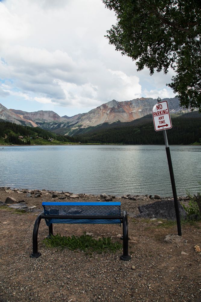 Lakeside bench overlooking mountain views with warning sign and rocky shoreline.