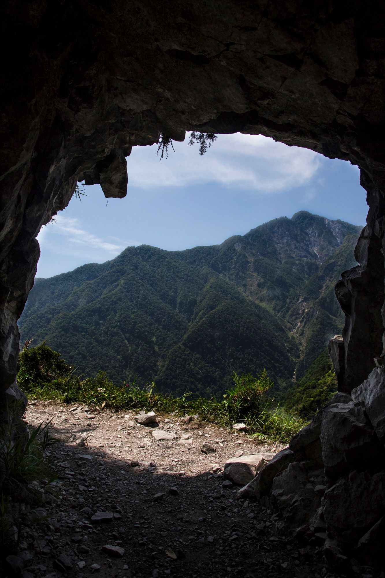 Mountain vista seen through a natural cave opening with sunlit peaks in the distance.