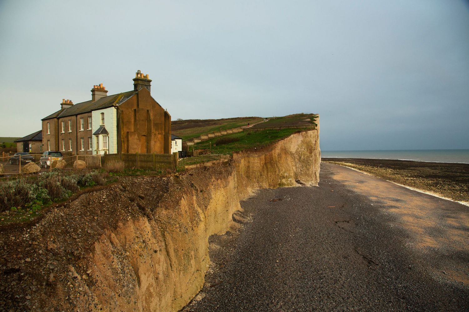 Coastal road winds along cliff edge with old brick buildings and dramatic ocean views.