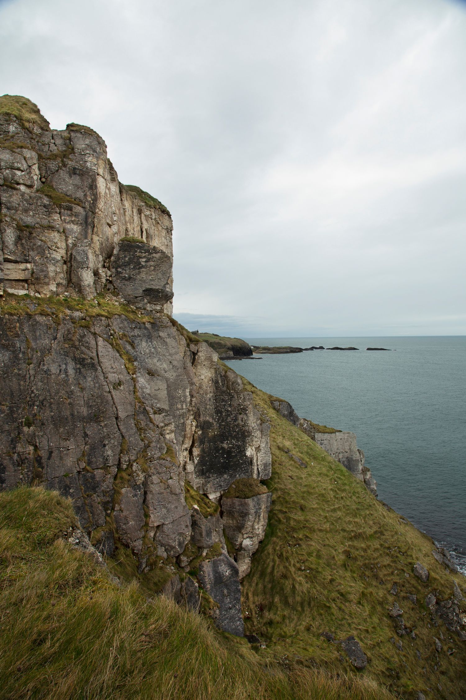 Steep coastal cliffs rise dramatically from the sea under overcast skies.
