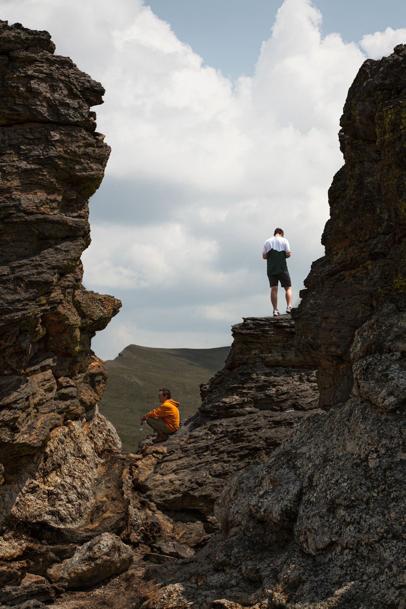 Hikers explore rugged rocky cliffs against a cloudy sky, showcasing the dramatic mountain landscape.