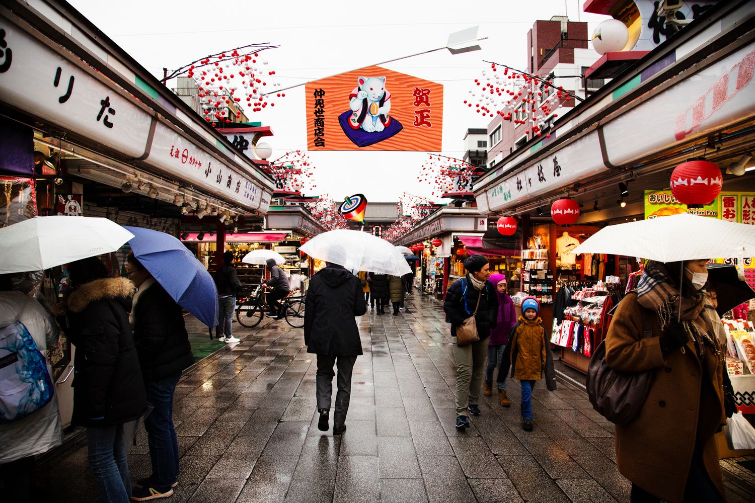 Traditional Japanese market street with red lanterns and umbrellas on a rainy day.