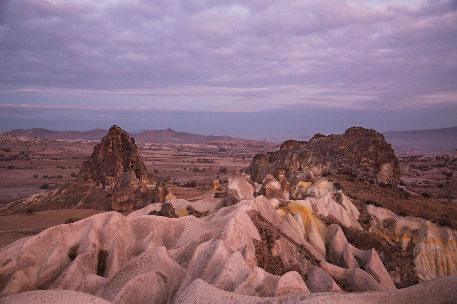 Dramatic rock formations rise from eroded landscape under moody purple skies in Cappadocia, Turkey.