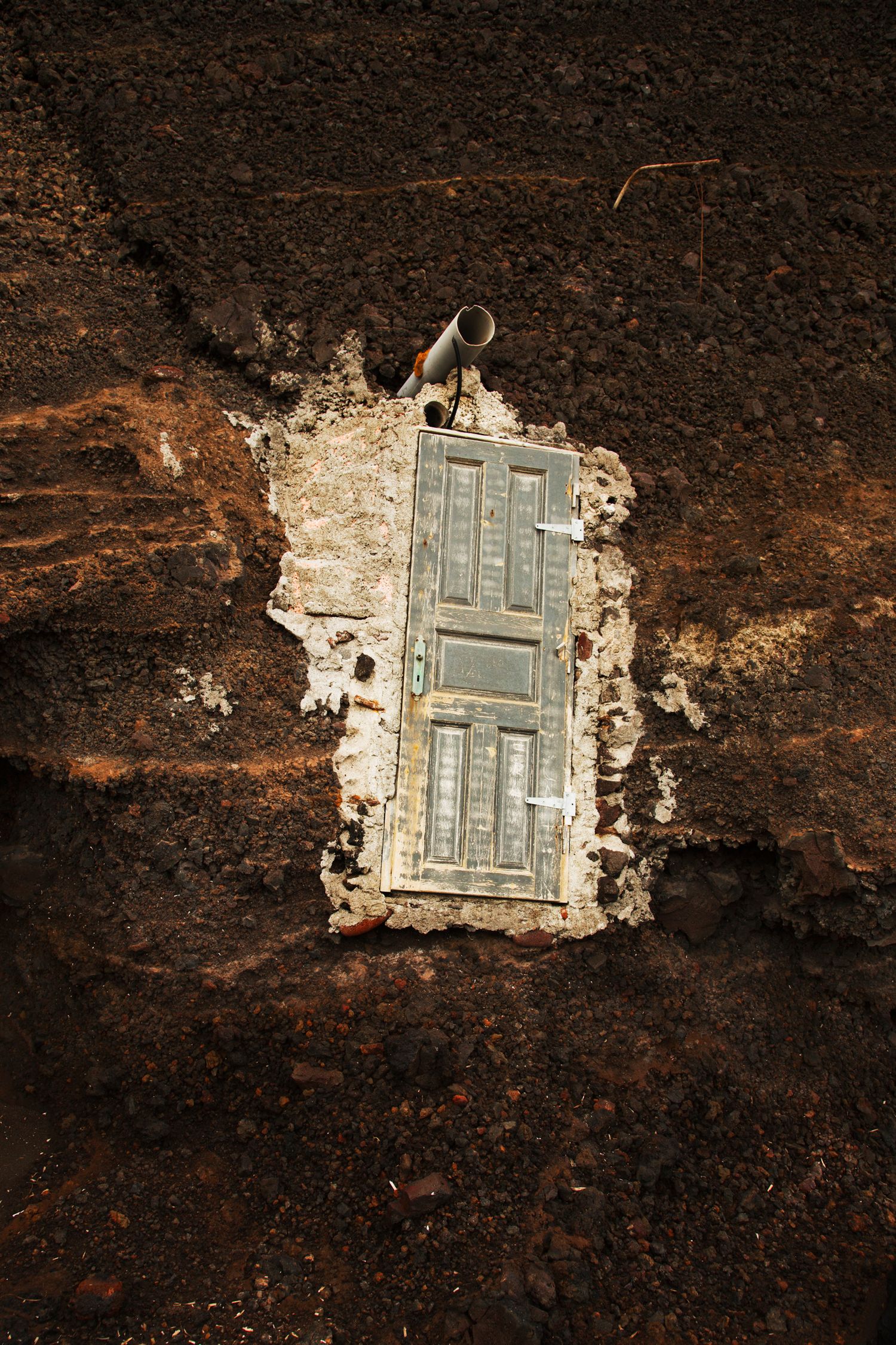 Abandoned door frame embedded in dark volcanic rock wall showing signs of decay.