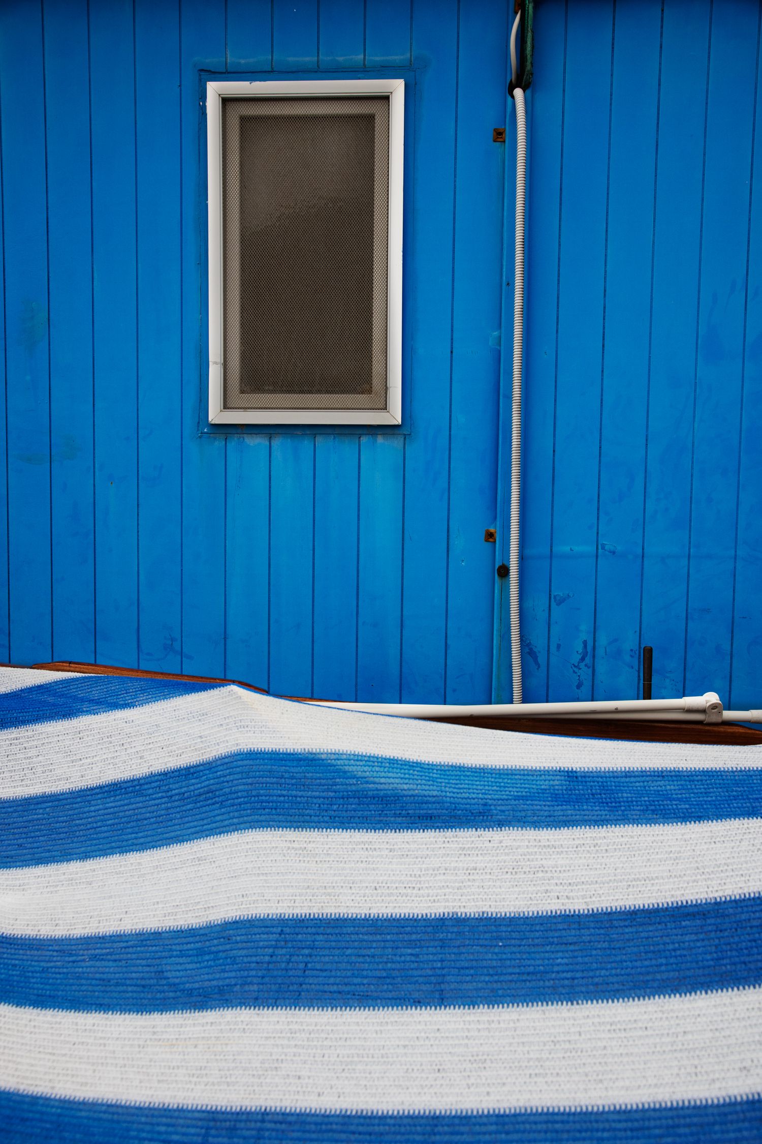 Blue striped fabric draped against a bright blue wooden wall with a small window outdoors.