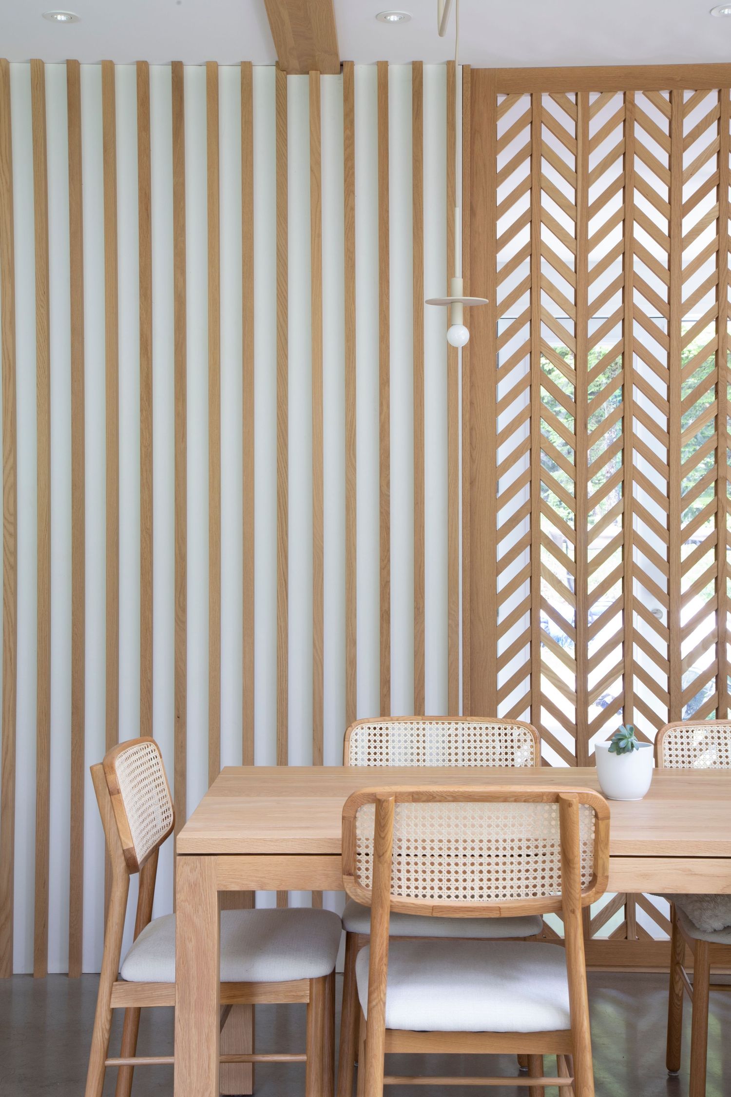 Row of contemporary wooden chairs with woven cane backs against a striped wall with geometric pattern screens.