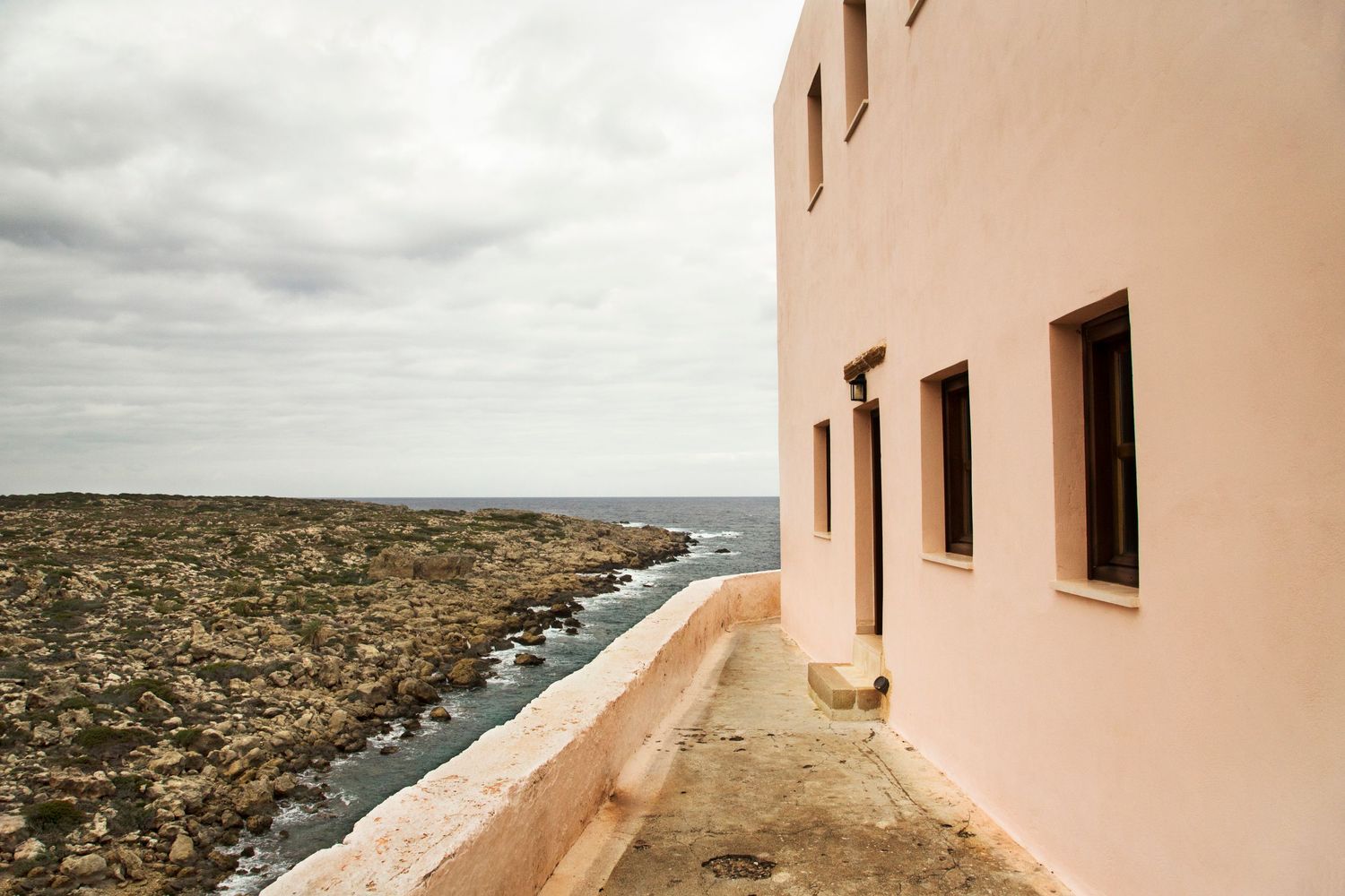 Coastal lighthouse building with pink walls overlooking rocky shoreline and ocean.