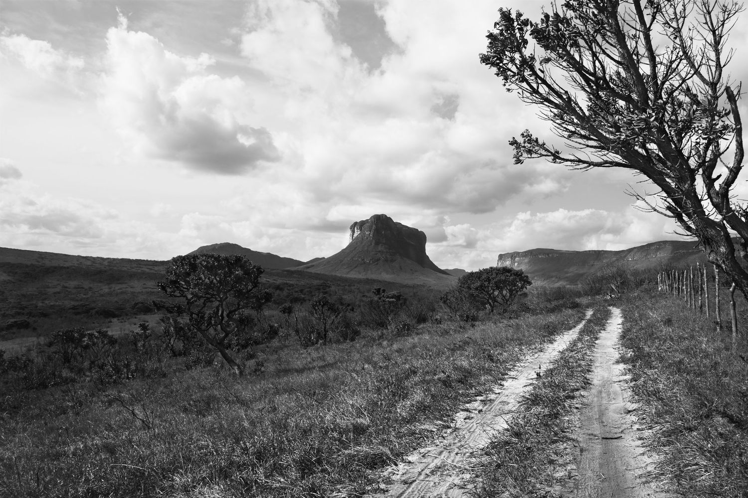 Winding dirt path through rugged mountain terrain with dramatic clouds overhead.
