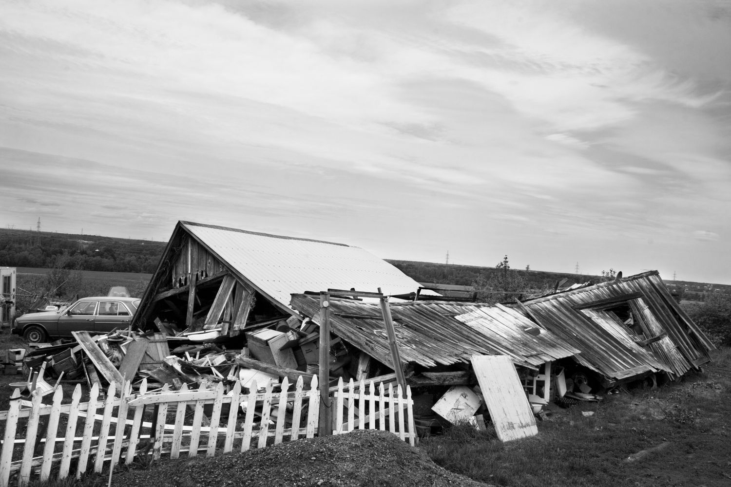 A panoramic black and white photograph shows a row of damaged buildings and debris after a natural disaster.