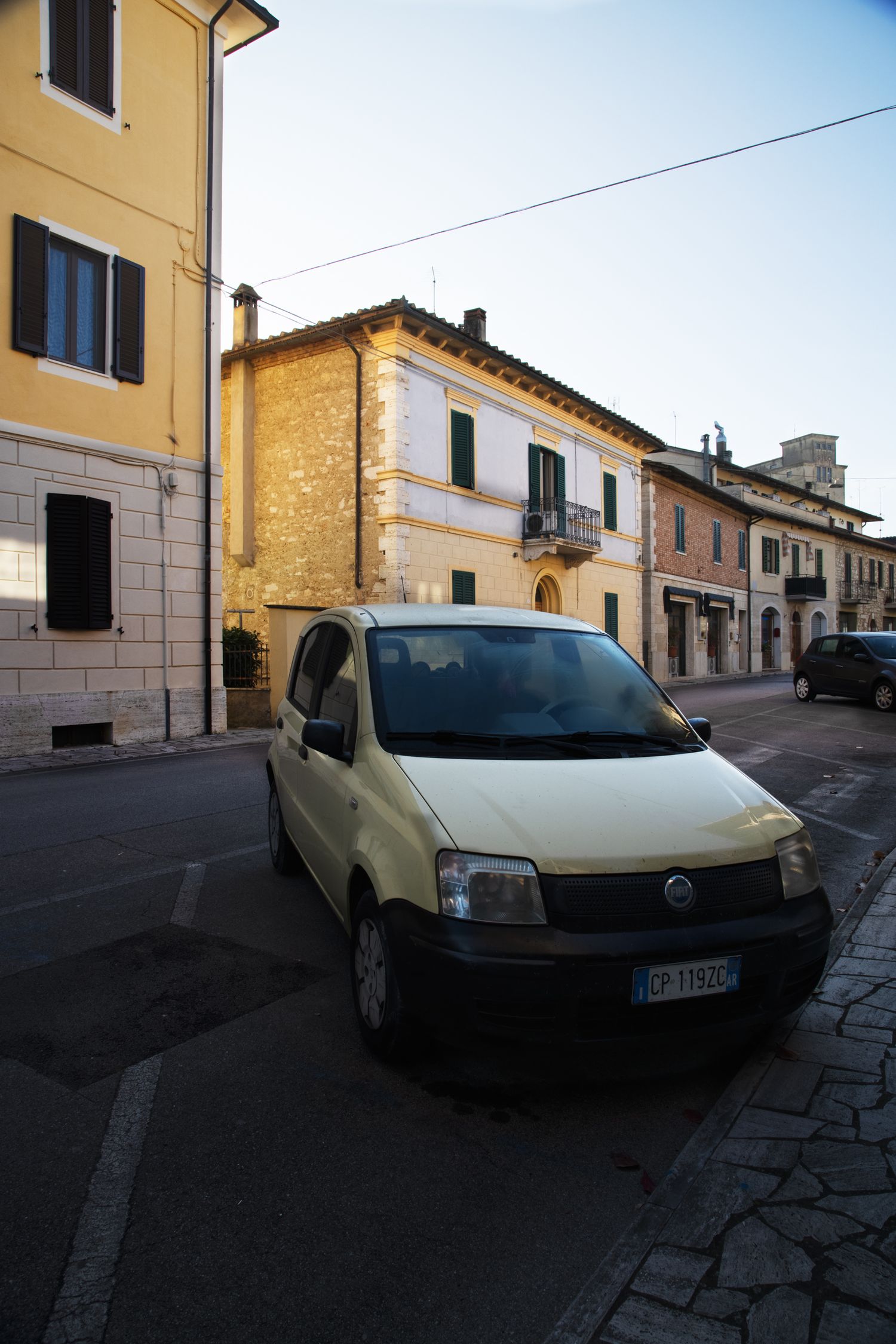 A yellow Fiat Panda parked on a narrow street in an Italian town with historic stone buildings.