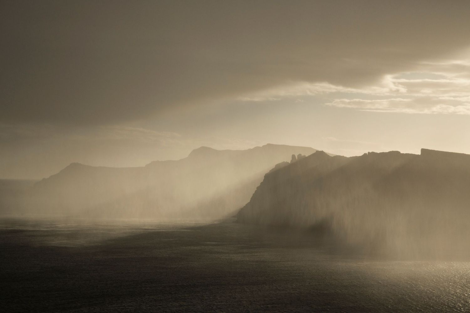 Misty mountain landscape at sunset with dramatic silhouettes against golden sky.