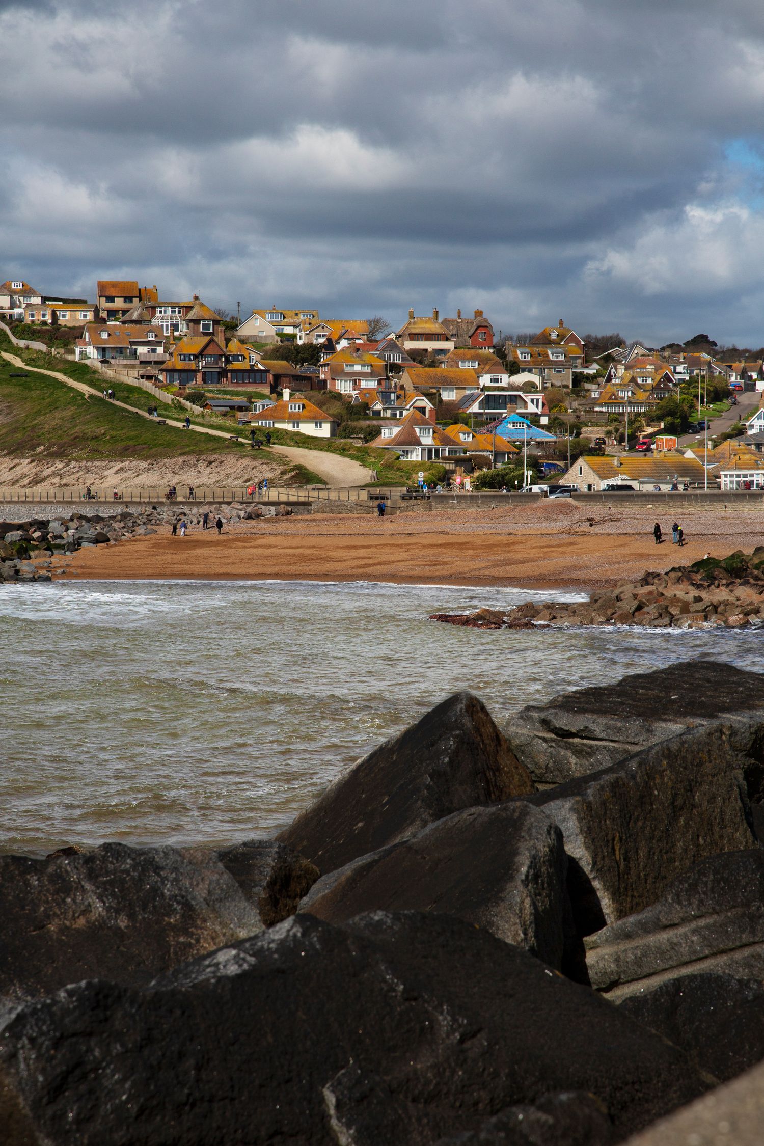 Coastal town houses clustered on hillside overlooking rocky beach with rough seas.