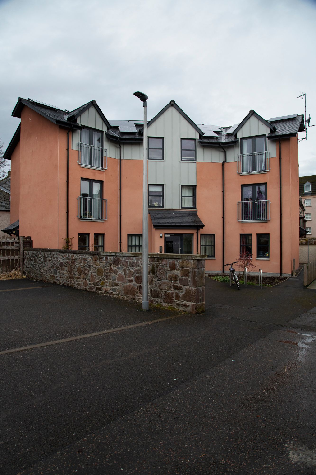 Modern townhouses with salmon-colored walls and gray roofs line a curved driveway against an overcast sky.