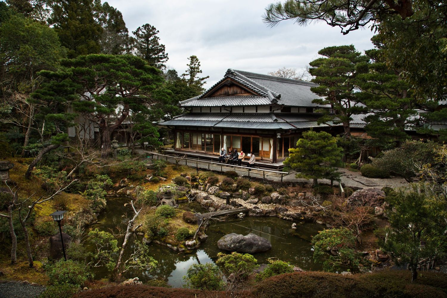 Traditional Japanese temple buildings nestled among trees in a panoramic landscape view.