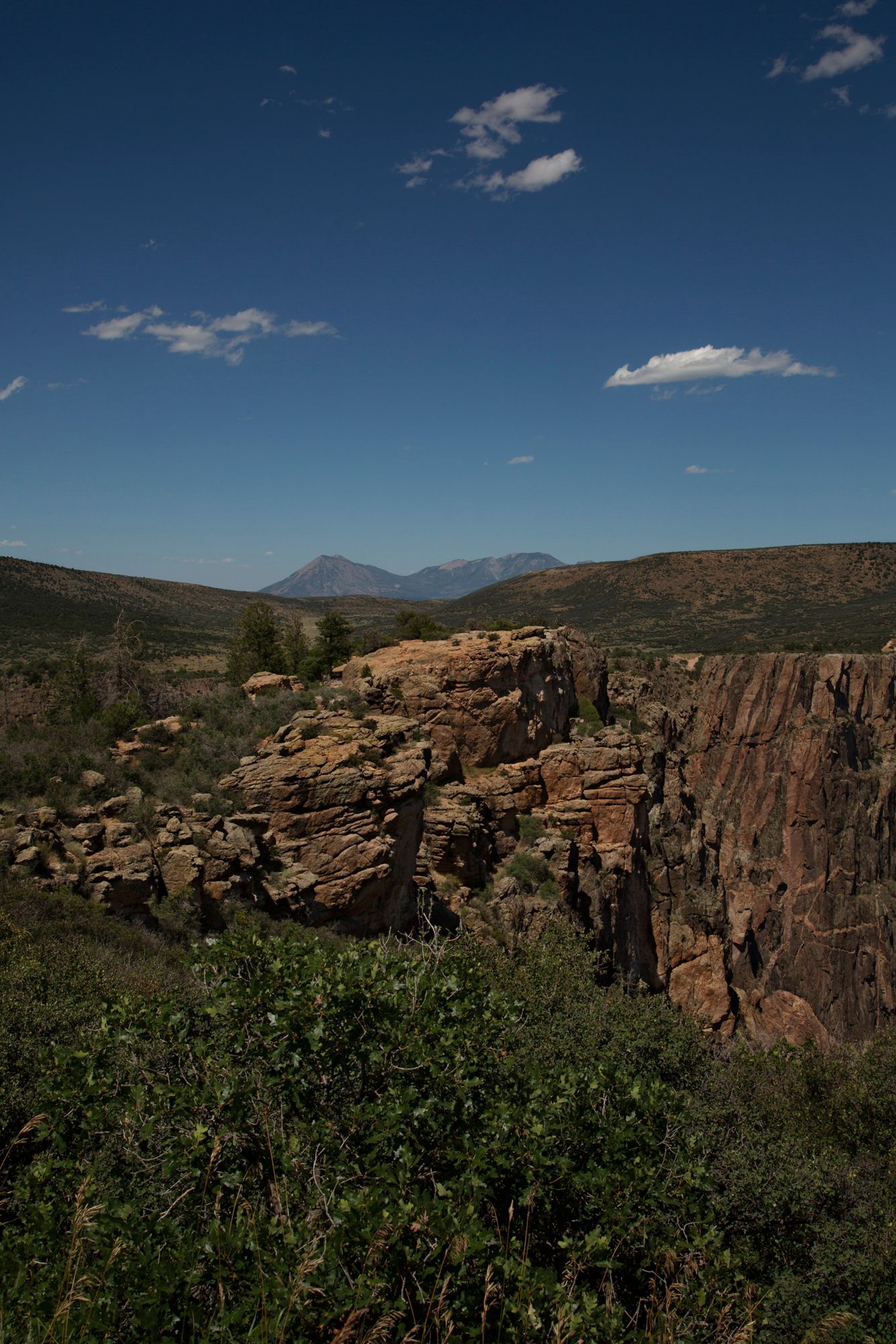 Dramatic rocky cliffs and rugged terrain against distant mountains under a deep blue sky with scattered clouds.