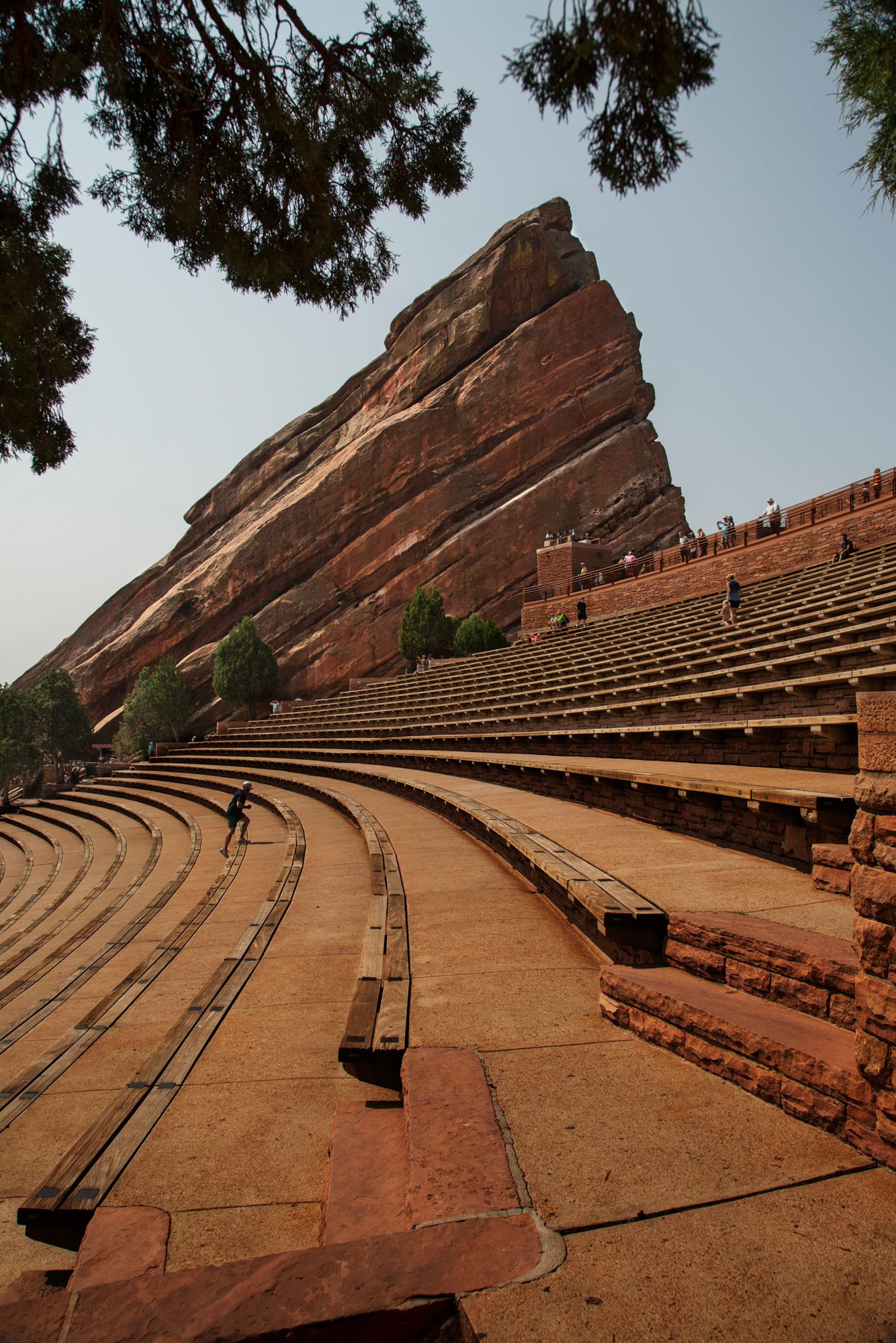 Red Rocks Amphitheatre's iconic sandstone seating area stretches upward against a cloudy Colorado sky.